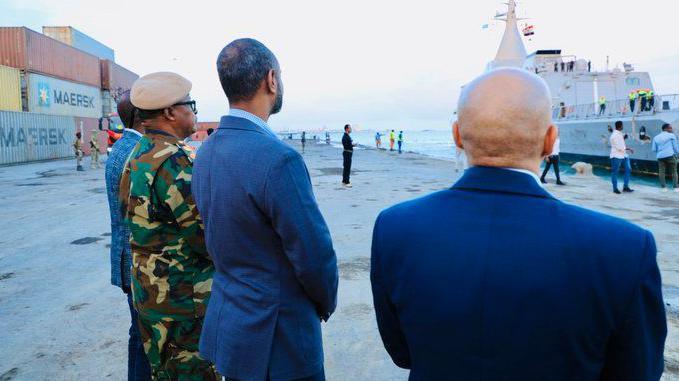 Four men with their backs to the camera looking at a ship in port