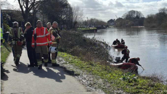 Emergency crews walk along the the riverbank while others are on boats on the water.