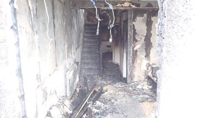 Interior of the house after the fire - the staircase is now burnt timbers and the floor is covered in ash and debris. 