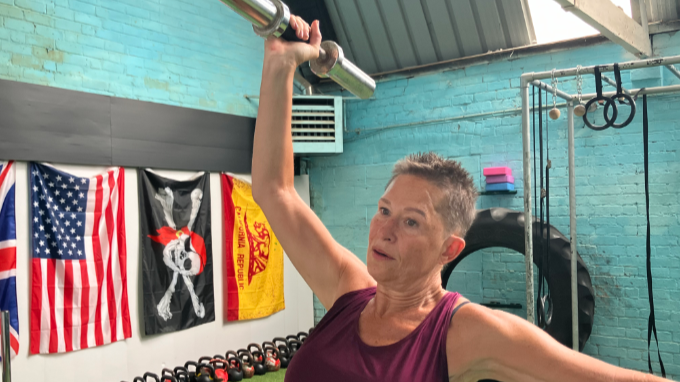 Zelda Wilson in the gym, she is lifting a barbell above her head with her right arm