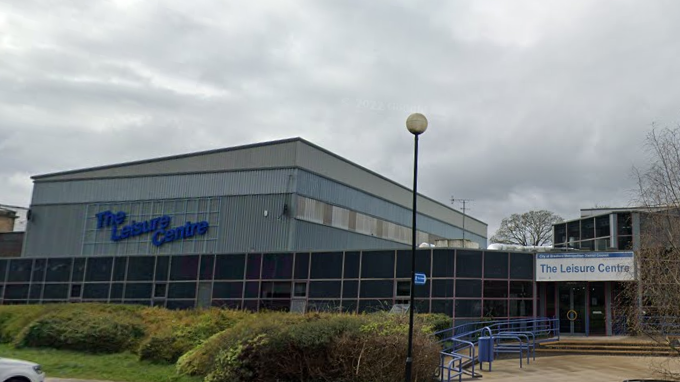 The front of the leisure centre, with ramps leading up to the entrance on the right, and a large blue sign on the hall to the left.