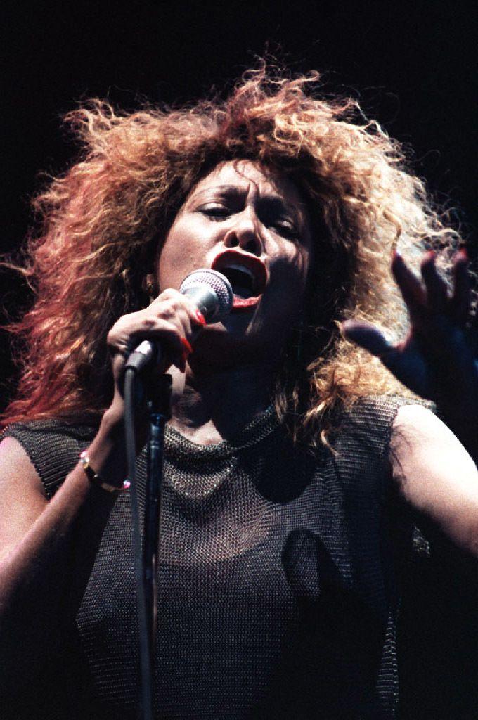 Tina Turner, in a sheer black dress, is illuminated by red and white lights as she performs on stage