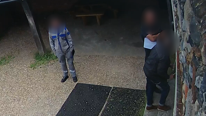 A CCTV image showing three men standing outside The Rehearsal Rooms studio. Their faces are blurred. They are standing in a courtyard area.
