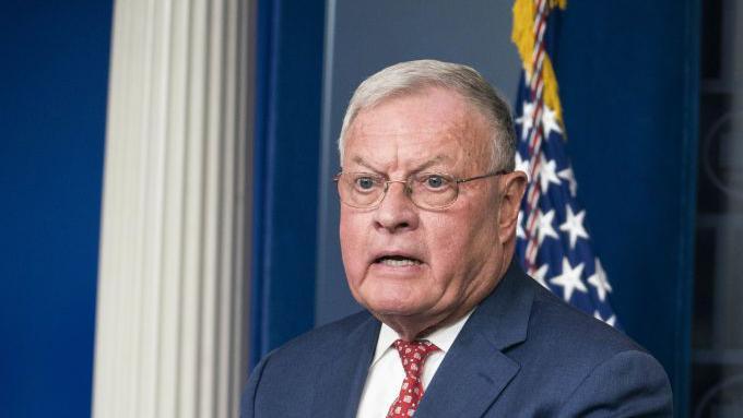 Keith Kellog, a grey-haired man wearing glasses, stands at the White House briefing room podium while wearing a navy suit, white shirt and red tie.