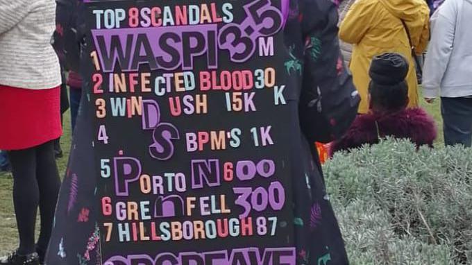 A woman during a Waspi protest in London during the autumn budget speech. She is wearing a black board notice over her back that details 'top eight scandals' with Waspi listed at the top.