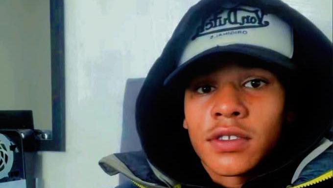 Devon Simmonds is wearing a baseball cap with his hood up. He is staring directly at the camera.