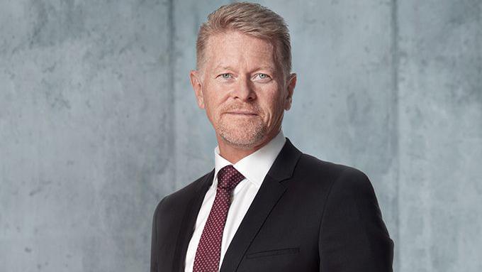 Studio publicity shot of Vestas' chief technology and operating officer Anders Nielsen. He is blond with pale blue eyes and is wearing a dark suit with a white shirt and red patterned tie.