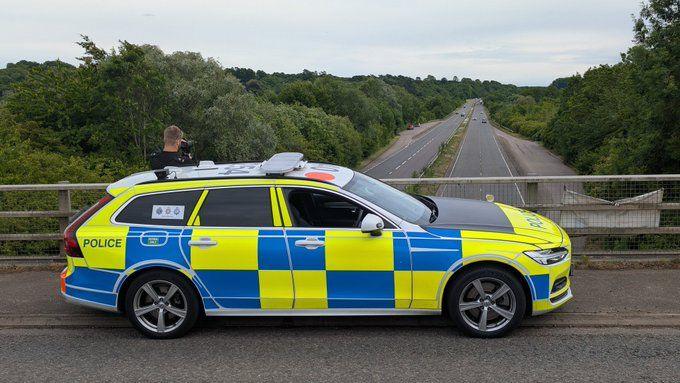 A police car is parked on a bridge overlooking a dual carrigeway