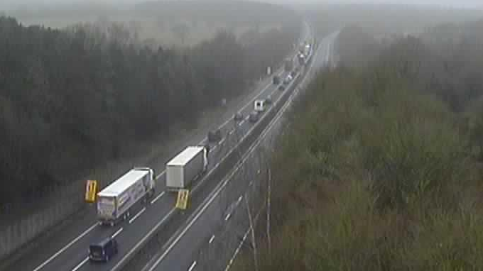 The M26 seen from above with lorries and cars travelling on one side of the road and an empty carriageway on the other side. There are trees either side.