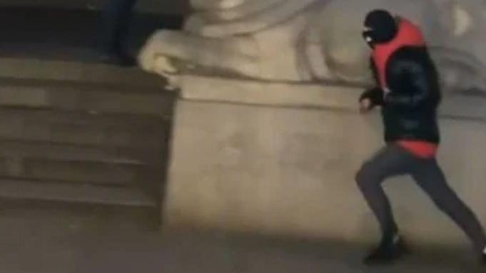 A young male running in front of the council house in Nottingham wearing a black padded coat with a red hoody underneath and a black balaclava