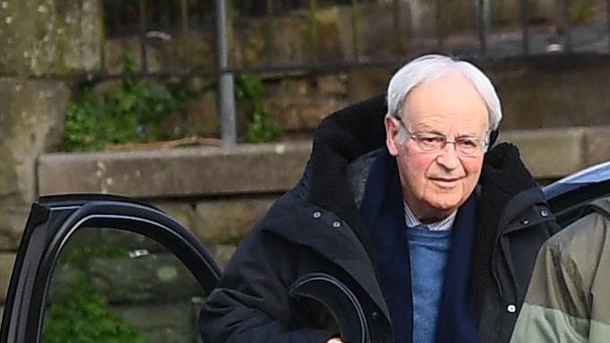 Anthony Pierce, who has white hair and glasses, wearing a blue sweatshirt and black coat, getting out of a car.