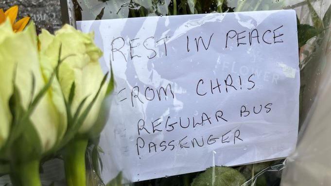 Written message amid flowers which reads: 'Rest in peace, from Chris, regular bus passenger'.