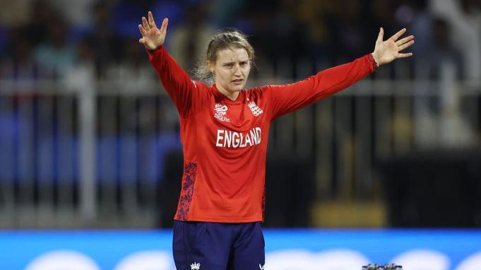 Charlie Dean holds her arms out in the air while playing for England