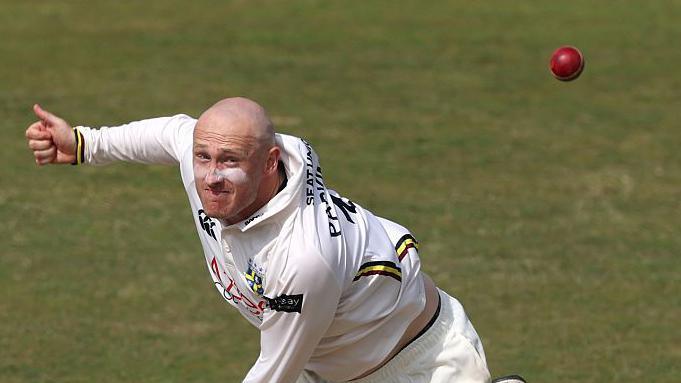 Left-arm spinner Callum Parkinson bowling a ball for Durham with the red cricket ball in the top right corner of the photo