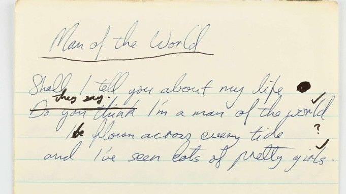 A close up image of a yellowed piece of lined paper with scrawled blue writing upon it which reads: "Man of the world." 