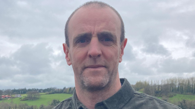 Shows a man in a dark shirt standing in front of fields
