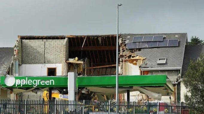 The aftermath of the explosion at the service station in Creeslough on 7 October 2022. A large hole can be seen in the roof of a nearby building to the Applegreen service station. 