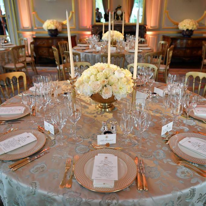 A round banquet table laid out for a dinner service with a round flower arrangement of white roses in the centre of the table