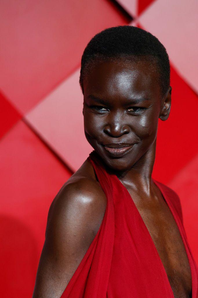 A tall, elegant woman in a red dress smiles on the red carpet.