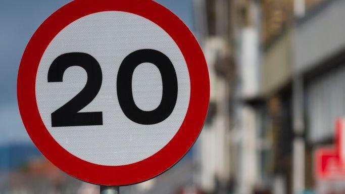 Picture of the 30mph road sign in a street. The background is heavily blurred. 