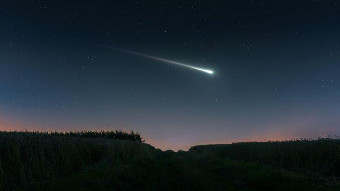 Bright shooting star in the evening sky over the fields.