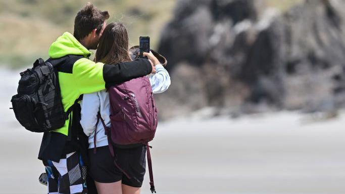 Visitors take selfies in front of a sea lion at Sandfly Bay in Dunedin