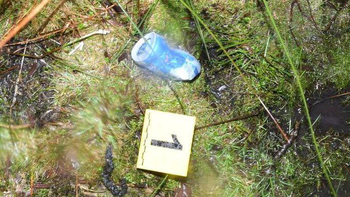 A crushed Red Bull can on a grassy piece of ground with a police evidence marker beside it