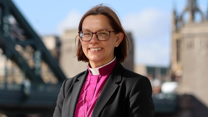 Bishop of Newcastle Helen-Ann Hartley wears a pink robe and brown glasses
