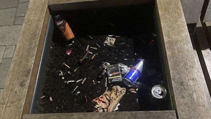 A planter filled with cigarette butts and litter