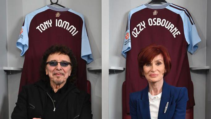 Tony Iommi in black shirt, jacket and dark glasses and Sharon Osbourne in navy suit jacket and white T-shirt sitting in a player's changing room at Villa Park. Two strips, in maroon and sky blue, are hung behind them both featuring the names Ozzy Osbourne and Tony Iommi on their backs.