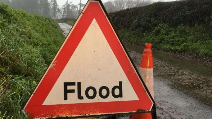 A file photo of a flood warning sign on a rural road - with an orange and white traffic cone next to it