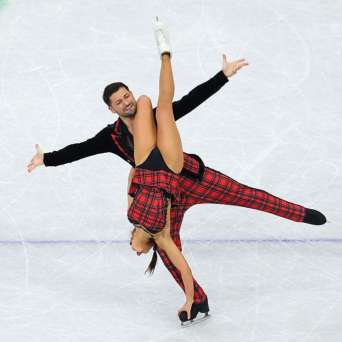 lilah holds onto lewis' skate upside down with her leg in the air.