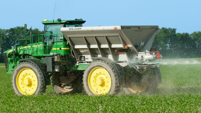 Agricultural machinery in a green field spraying fertiliser onto the field.