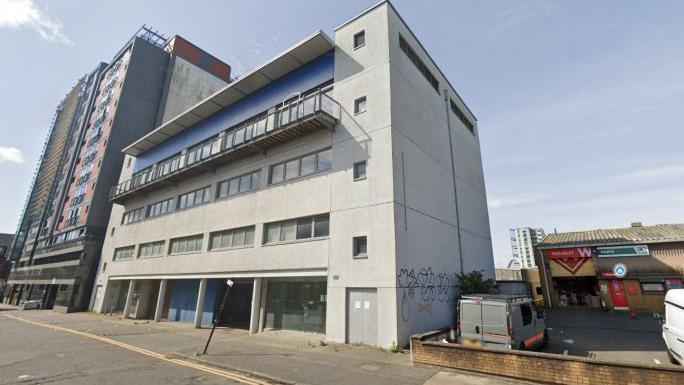 A grey four storey office building. There is graffiti on the sides and it looks run down. 