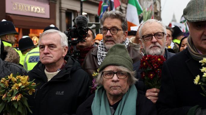 Jeremy Corbyn (second from right) and John McDonnell (far left) carry flowers as they join a PSC rally in central London on Saturday 