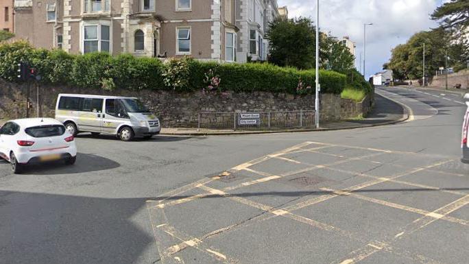 A Google Maps image shows the junction with yellow crosshatching across the middle. Two vehicles are on the left while a building can be seen in the background. 