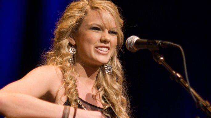 Taylor in 2007 with a microphone, curly hair and long earrings