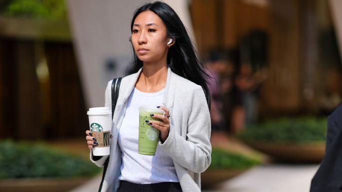 Woman carrying two Starbucks drinks and walking down street