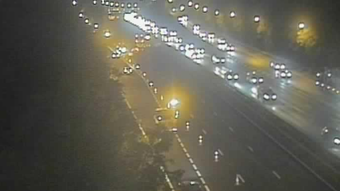 A traffic camera image of the M1 northbound carriageway near Watford. The carriageway can be seen cordoned off with cones as drivers divert off a slip road. Traffic can be seen moving past on the opposite carriageway. It is dark and headlights as well as street lights can be seen.