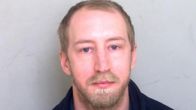 Custody mugshot of Brett Baker, who is looking at the camera, expressionless.