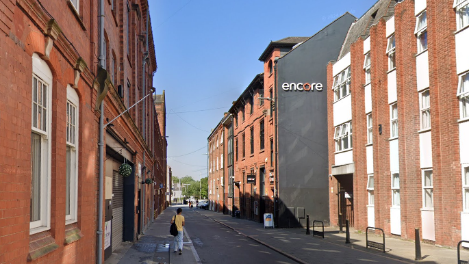 A street view of Millstone Lane in Leicester showing the Encore student flats building on the right and a person walking along the pavement on the left