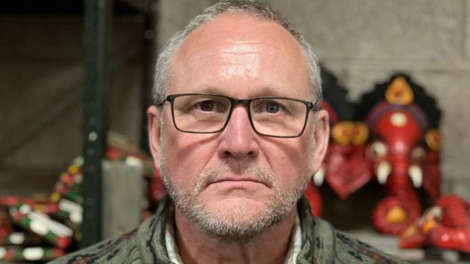 Bernard Rostron. He has short grey hair and beard with black-framed glasses