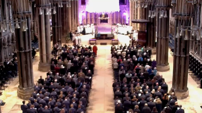 A view from high up in the Cathedral, looking down towards the altar, with seated worshipers either side of the building. The altar is lit up in purple.