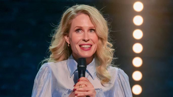 Lucy Beaumont smile wearing a blue blouse holding a black microphone as she hosts the BBC New Comedy Award Finals at The Alexandra Theatre in Birmingham in 2024.