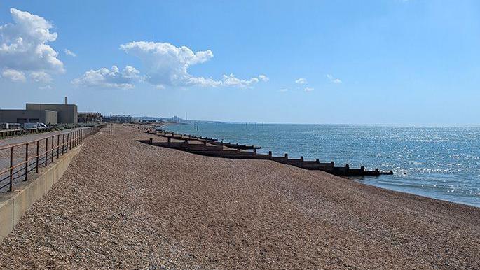 A shingle beach with groynes. There is a promenade running behind the beach.
