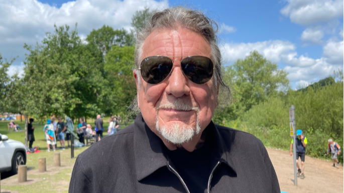 Robert wears a black top and jacket and sunglasses. His hair is tied back.