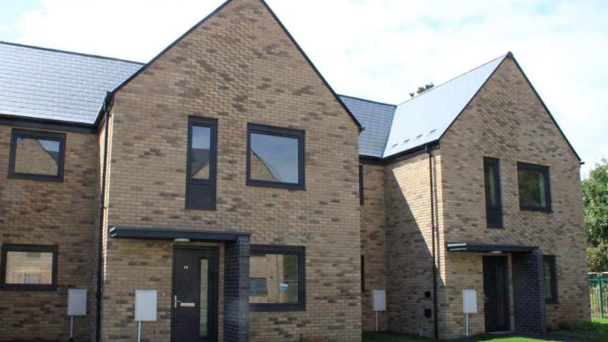 Two beige brick new-build terraced homes with black window frames, roofs and front doors