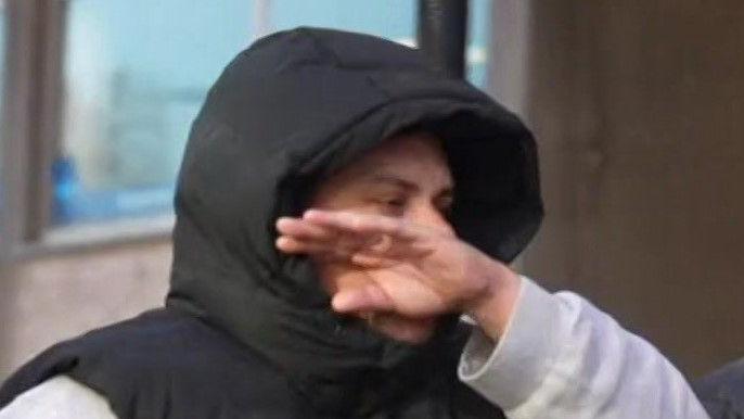 Dominic D'Sa: a man wearing a black, sleeveless, hooded top over a pale sweatshirt. He is holding his left arm across his face. 