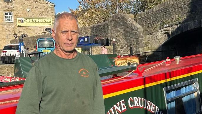 Ian Clarke, director of Pennine Cruisers, standing in front of one of his boats with a canal bridge in the background.