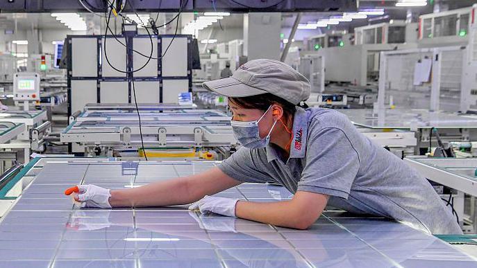 A woman leans over a large sheet of solar panel modules at a factory in Jinhua, Zhejiang Province of China. 